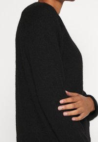 Schwarzer Strickpullover mit langen Ärmeln, einem runden Ausschnitt und weichem, strukturiertem Stoff, der ein entspanntes Design präsentiert.