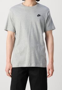 Šedé tričko vyrobené z bavlny, se žebrovaným kulatým výstřihem a malým černým logem Nike na levé horní části hrudníku.