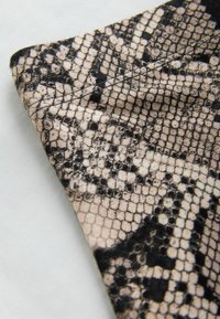 Tissu beige et noir avec un motif texturé de peau de serpent, plié sur une surface gris clair.