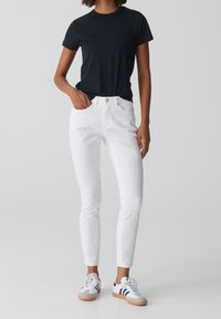 Jeans blancos ajustados con una textura suave, combinados con una camiseta negra de manga corta. Usados con zapatillas blancas y grises con rayas azules.