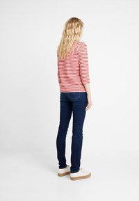 Rot-weiß gestreiftes Langarmshirt kombiniert mit dunkelblauen Jeans und weißen Schuhen, Ansicht von hinten.