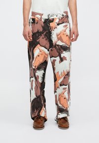 Nyomott nadrág, változatos ló grafikával a földszínek árnyalataiban. Lazán illeszkedő fazon, puha anyagból készült, derékpánttal és övhurkokkal.