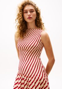 Robe rayée avec un corsage ajusté en tissu rouge et crème, arborant des rayures horizontales et verticales, et un bas plissé.