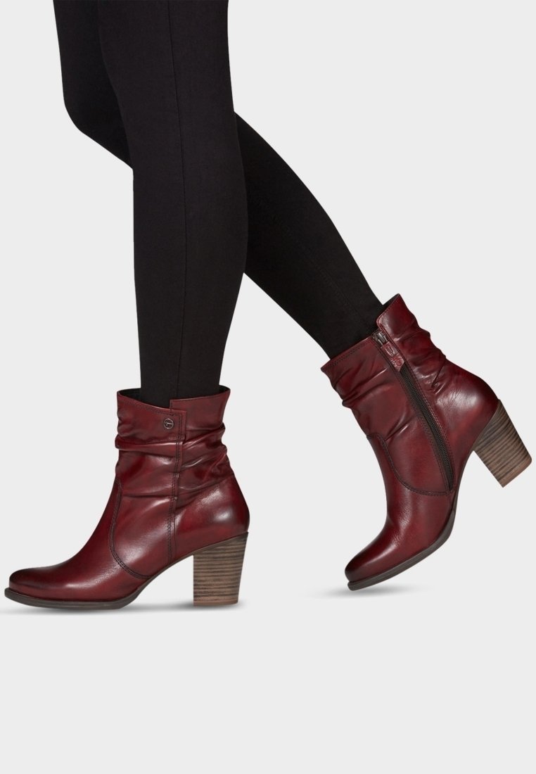 Femme portant des leggings noirs et des bottines en cuir rouge foncé avec talons en bois empilés et fermetures éclair latérales.