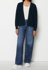 Mörkgrön stickad cardigan med öppen front, kombinerad med ljusblå vida jeans och vita sneakers. En enkel och avslappnad silhuett.