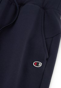 Granatowe dresy z miękkiego materiału, z elastycznym pasem, bocznymi kieszeniami i małym haftowanym logo na lewym udzie.