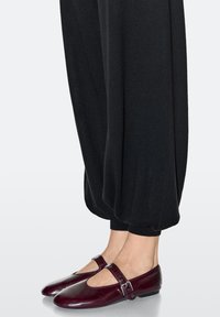 Bordeauxrode leren Mary Jane platte schoenen met een ronde neus en een enkele gesp, gecombineerd met zwarte, loszittende broek.