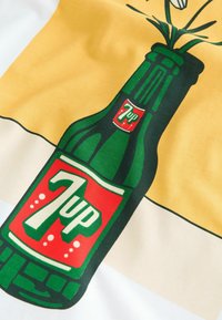 Bouteille verte de 7up avec une étiquette rouge posée sur un fond en tissu rayé jaune et blanc.