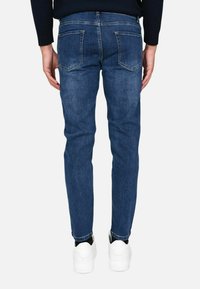 Jeans in denim blu scuro con una vestibilità slim, dotati di due tasche posteriori, cuciture visibili e orli risvoltati, abbinati a sneakers bianche.