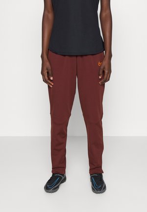 Pantaloni sportivi bordeaux con una vestibilità comoda, presentano un logo arancione sul davanti e un tessuto traspirante. Scarpe nere con dettagli blu.