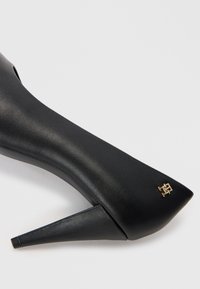 Sort højhælet sko lavet af glat læder, med spids tå og trekantet stiletto hæl. Guld hardware detalje.