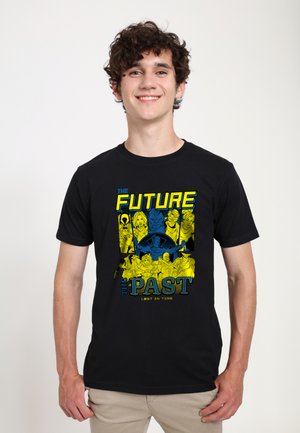 Giovane uomo che indossa una maglietta nera con personaggi in stile fumetto e testo "The Future The Past Lost in Time" in colori giallo e blu.