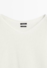 White cotton knit sweater featuring a V-neckline and a textured, breathable fabric. Labels indicate brand and material composition.