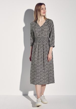 Abito a maniche lunghe con scollatura a V e vita smock, caratterizzato da un motivo floreale bianco e nero. Indossato con sneaker bianche.