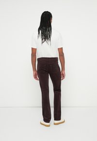 Pantalone od kordura u dubokoj burgundi boji s ravnim krojem, s nazadnim džepovima i teksturiranim završetkom, upareni s bijelim tenisicama.