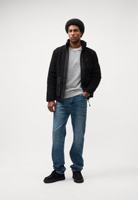 Giacca in pile nera con tasca con zip, felpa grigia, jeans blu e sneaker nere. Tessuti in misto cotone, vestibilità comoda e dettagli texturizzati.