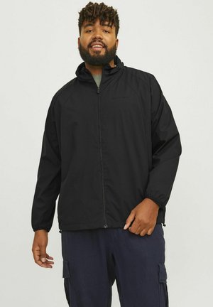 Black lightweight jacket with a full zipper, high collar, and elastic cuffs. Worn over a green shirt, paired with dark cargo pants.