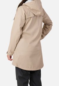 Veste imperméable beige avec capuche, présentant une coupe décontractée, des poignets à boutons-pression et une texture lisse. Vue de dos mettant en valeur la longueur et le design.