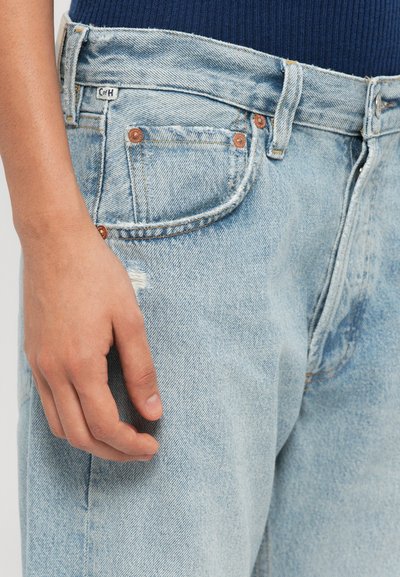 Light blue denim jeans with a relaxed fit, featuring a distressed detail on the thigh, copper rivets, and a label sewn into the waistband.