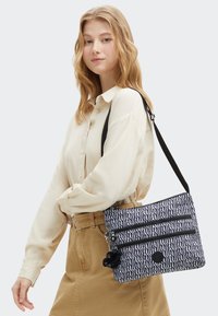 Borsa a spalla a fantasia bianca e nera con due scomparti con cerniera, realizzata in tessuto, con un charm a pom-pom e un logo circolare.