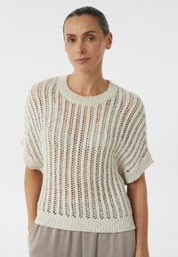 Sweter z dzianiny o luźnym splotu w odcieniu kremowym, z krótkimi rękawami i ściągaczem przy dekolcie. Ma poziome paski i swobodny krój.