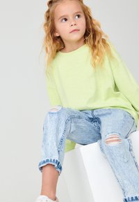 Felpa oversize verde chiaro con scollatura rotonda, abbinata a jeans azzurri chiari strappati con orli sfrangiati e ginocchia strappate.