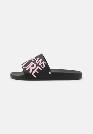Sort slidesandal med bred rem med stor pink tekst, flad sål og tekstureret fodseng på hvid baggrund.