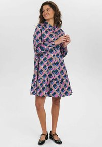 Un vestito viola con un motivo geometrico in rosa, blu e nero; presenta un colletto, una chiusura con bottoni davanti e una gonna svasata con rouches.