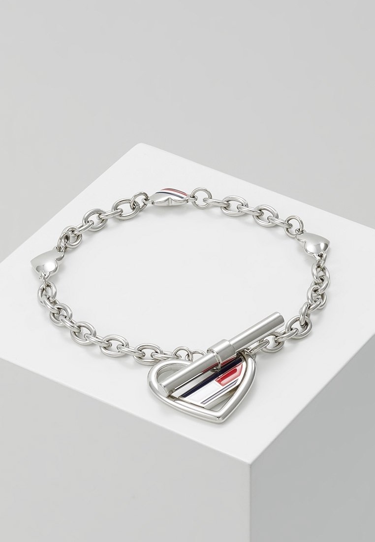 Bracelet chaîne en argent avec fermoir toggle en forme de cœur avec des rayures en émail rouge, blanc et bleu sur un bloc d'exposition blanc.