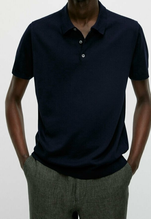 Polo marine à manches courtes avec patte de boutonnage à trois boutons, texture douce, associé à un pantalon texturé gris clair.