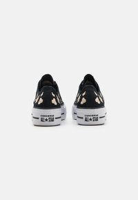 Fekete vászon tornacipők fehér gumitalppal, pöttyös mintával és "CONVERSE ALL STAR" felirattal a saroknál.