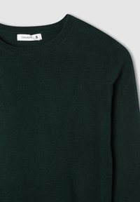 Ciemnozielony sweter z dzianiny z okrągłym dekoltem i ściągaczami, wyeksponowany na jasnoszarym tle. Metka pokazuje rozmiar "S".