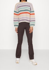 Strikket sweater med pastelfarvede striber i orange, grøn og lilla. Sammen med brune tætsiddende bukser og lyse sneakers. Tekstureret stof.