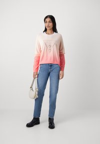 Felpa con gradiente rosa chiaro e corallo con logo "GUESS U.S.A.", abbinata a jeans in denim blu e stivaletti neri alla caviglia. Borsa bianca inclusa.