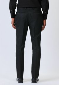 Pantaloni neri con motivo a diamante, dotati di due tasche posteriori e una vestibilità sartoriale. Il materiale ha una texture liscia.