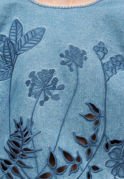 Haut en denim avec des motifs floraux brodés en bleu foncé, un col rond et des découpes le long de l'ourlet pour plus de détails.