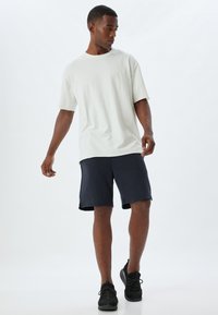 Ljust grå överdimensionerad T-shirt med uppvikt ärm, i kombination med mörkblå shorts. Modellen bär svarta sneakers. Enkelt mönster, minimal dekoration.