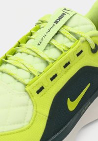 Nike sneaker met een levendige lime groene bovenkant met een geborduurde textuur, contrasterende donkerblauwe accenten en een opvallend swoosh-logo in groen.