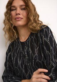 Blusa patterned in bianco e nero con scollo rotondo, chiusura a bottoni e tessuto texturizzato. Presenta una vestibilità ampia e maniche lunghe.