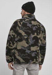 Camouflage fleece jacket in dark green, gray, and beige tones. Features a high collar and textured, soft surface. Back view shows simple design.