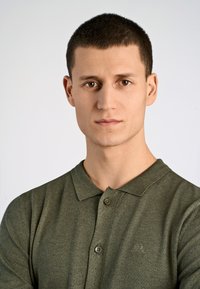 Zielona koszulka polo z krótkim rękawem, z kołnierzykiem i dwoma guzikami, wykonana z teksturowanej tkaniny, z małym haftem logo.