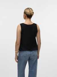 Top nero senza maniche con scollatura rotonda, abbinato a jeans in denim blu larghi. Tessuto morbido e design semplice, senza motivi visibili.