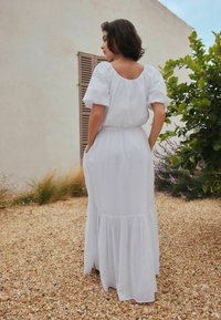 Vestido blanco hasta los tobillos, hecho de tela ligera, con mangas cortas abullonadas, cintura fruncida y dobladillo escalonado.