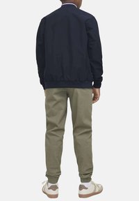 Giacca bombardiere navy con colletto a coste, abbinata a pantaloni tapered di un verde oliva chiaro. Indossata con scarpe da ginnastica bianche e beige, che mostrano polsini elastici.