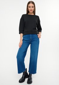 Schwarzer Baumwoll-oversized Sweatshirt mit Dreiviertelärmeln, kombiniert mit blauen, weit geschnittenen Jeans und schwarzen klobigen Stiefeletten.