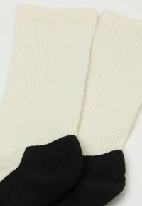 Calcetines acanalados en color crema con un puño negro de contraste. Tejido suave, con punta redondeada y un diseño simple y funcional.