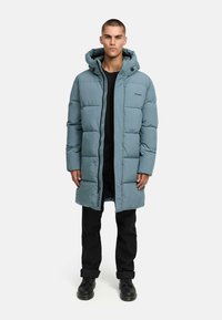 Light blue puffer coat with a hood, featuring a full front zipper, quilted design, and side pockets. Worn over a black top and pants.