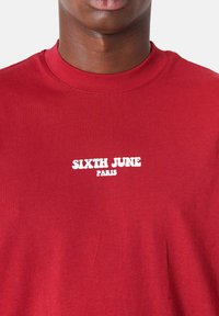 Rode katoenen t-shirt met een geribbelde halslijn en witte opdruk "SIXTH JUNE PARIS" op de voorkant, die een gladde textuur toont.