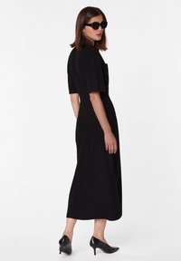 Robe noire à manches courtes, corsage ajusté et jupe fluide. Modèle associé à des lunettes de soleil noires et des talons aiguilles. Texture lisse.