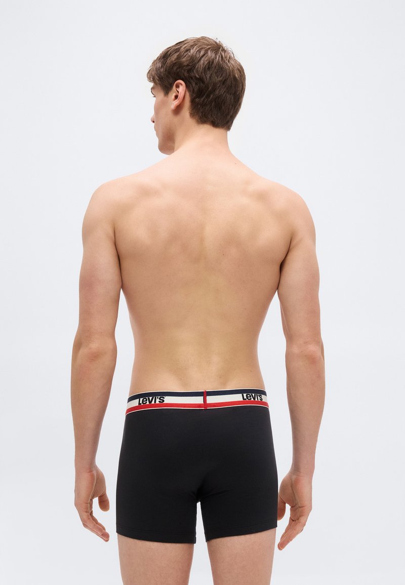 Young man standing shirtless facing away, wearing black Levi's boxer briefs with white and red waistband.